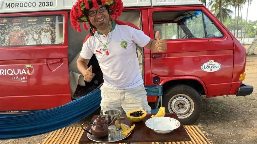 Image de Football. Les supporters marocains démontrent une passion inébranlable pour leur équipe nationale de football, les Lions de l’Atlas, lors de la Coupe d’Afrique des Nations en Côte d’Ivoire. Parmi eux se trouve Aznzar, un fervent supporter qui a entrepris un voyage épique de 6000 kilomètres à travers cinq pays en cinq mois pour soutenir son équipe. Aznzar, un homme au van faisant face à l'océan Atlantique à San Pedro, incarne l'engagement sans faille des supporters marocains. Sa présence dans la ville suscite l'admiration et l'intérêt, attirant l'attention des habitants locaux ainsi que des supporters d'autres pays. Son voyage, tout comme celui d'autres supporters marocains, illustre leur dévouement envers leur équipe nationale. La mobilisation des supporters marocains dépasse largement le simple soutien lors des matchs. Certains ont entrepris des voyages audacieux, tels que celui à vélo ou en Renault 4L, pour atteindre San Pedro. Leur détermination à être présents pour soutenir les Lions de l’Atlas reflète l'importance du football dans la société marocaine et la solidarité entre les supporters. Pour Aznzar, ce voyage est bien plus qu'une simple démonstration d'amour pour le football. Il utilise cette expérience pour interagir avec les populations locales, distribuer des ballons et des stylos aux enfants, et promouvoir un message de solidarité africaine. Son engagement dépasse les frontières du sport, témoignant de sa conviction en la capacité de l'Afrique à se soutenir mutuellement et à développer ses talents. À travers ses voyages pour soutenir les Lions de l’Atlas, Aznzar aspire également à sensibiliser aux besoins des jeunes talents africains en matière d'infrastructures sportives et d'opportunités. Il appelle à la création d'académies de football sur le continent pour exploiter le potentiel des enfants talentueux. Son initiative reflète l'importance du sport comme outil de développement social et d'épanouissement individuel. Alors que la compétition avance, Aznzar et d'autres supporters marocains croisent les doigts pour une victoire finale des Lions de l’Atlas. Leur engagement et leur dévouement sont une source d'inspiration pour les joueurs et pour toute la nation marocaine. Leur présence en Côte d’Ivoire ne se limite pas à un simple soutien sportif, mais constitue également un témoignage de l'unité et de la solidarité qui transcendent les frontières nationales. À la lumière de cet engagement exceptionnel, une question demeure : comment les expériences des supporters comme Aznzar peuvent-elles contribuer à renforcer les liens entre les pays africains et à promouvoir le développement du sport sur le continent ?