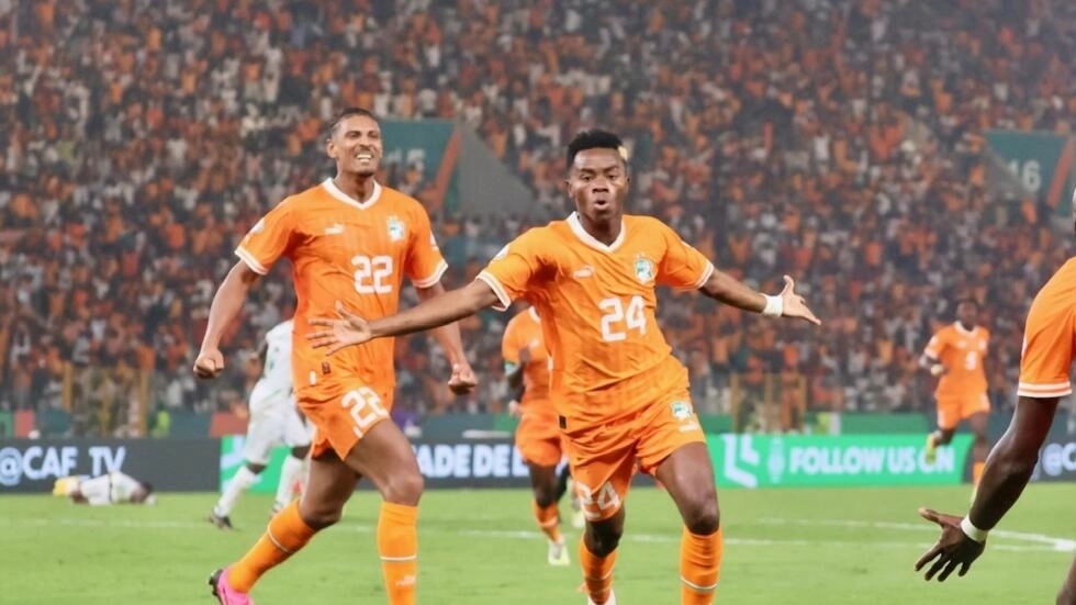 Image de Football. Le parcours épique de la Côte d'Ivoire à la CAN 2023 a trouvé son héros inattendu en la personne de Simon Adingra. Face au Mali en quart de finale, son but salvateur a non seulement égalisé le score, mais a également insufflé une nouvelle vie au rêve ivoirien de décrocher une troisième étoile. À 22 ans, le natif de Yamoussoukro devient le chaînon manquant que les Éléphants n'auraient jamais imaginé nécessaire. Un Moment Historique Le but mémorable inscrit par Adingra dans les derniers instants du temps réglementaire contre le Mali restera gravé dans l'histoire du football ivoirien. Ce moment de génie a déclenché une vague d'émotions incontrôlables, illuminant le stade de Bouaké d'une intensité rarement vue. Adingra lui-même, encore sous le choc de cet exploit, témoigne : "C'était incroyable, je ne peux pas expliquer ce que j'ai ressenti. Ça monte, ça descend, c’est incroyable." Coup de Maître du Sélectionneur Le conte de fées d'Adingra aurait pu ne jamais se concrétiser. À deux doigts de manquer la CAN en raison d'une blessure aux ischios, sa présence dans la liste des 27 joueurs sélectionnés était une audacieuse décision du sélectionneur ivoirien, Jean-Louis Gasset. Malgré le délai minimal de récupération, Gasset a fait preuve d'un flair remarquable en faisant confiance à Adingra. L'entraîneur peut aujourd'hui se féliciter de cette prise de risque payante. Détermination Personnelle La rapide guérison d'Adingra et sa performance décisive sont le résultat de sa détermination personnelle. Face aux spéculations sur une possible rétention par son club Brighton (Premier League anglaise), Adingra a dissipé les doutes en publiant un message rassurant à ses supporters. "Les rumeurs selon lesquelles Brighton me retiendrait sont complètement fausses. Je suis motivé pour représenter mon pays. Je travaille extrêmement dur chaque jour pour me remettre de ma blessure", a-t-il affirmé avec assurance fin décembre. Impuissance dans l'Attente La période d'attente, marquée par l'impuissance de ne pouvoir contribuer sur le terrain, a été une épreuve pour Adingra. Son équipe a traversé des moments difficiles au premier tour, et lui-même, en convalescence, a dû regarder depuis les tribunes. Sa première apparition dans la compétition, à la 87e minute face à la Guinée équatoriale, s'est terminée par des larmes, témoignant de l'émotion intense qui accompagne ce parcours. De la Convalescence à la Consécration Aujourd'hui, le sourire est de retour sur le visage d'Adingra. Depuis sa première convocation avec les Éléphants en juillet 2023, ce jeune attaquant est passé d'une période de convalescence émotionnelle à une consécration sur le terrain. Un journaliste ivoirien l'a affectueusement qualifié de "petit héros", une étiquette qui semble désormais coller parfaitement à son parcours. Une Ascension Déterminante Après des débuts convaincants en huitièmes de finale contre le Sénégal, suivi d'un impact décisif face au Mali en quarts de finale, Adingra se profile comme un élément clé pour la demi-finale contre la RD Congo. Malgré ses 71 minutes de jeu limitées depuis le début de la CAN, Adingra ne montre aucun signe de ralentissement. "On n'est pas venus jusqu’ici pour s’arrêter. On veut aller en finale", déclare-t-il avec détermination après la qualification des Éléphants dans le dernier carré. Quelle Suite pour l'Histoire d'Adingra ? La saga captivante de Simon Adingra, du bord du terrain à la position de héros national, soulève la question cruciale de ce parcours remarquable : quel sera le prochain chapitre de cette histoire ? Alors que les Éléphants se préparent pour la demi-finale contre la RD Congo, la performance d'Adingra pourrait bien être le facteur décisif dans la quête de la Côte d'Ivoire pour une troisième étoile. L'avenir de ce "petit héros" continue d'alimenter l'excitation des supporters et de susciter l'admiration du monde du football.