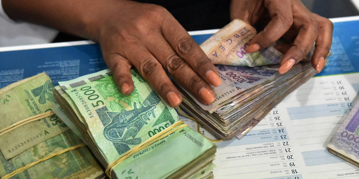 Image de Société. Depuis le 16 juillet 2024, la Banque Centrale des États de l'Afrique de l'Ouest (BCEAO) a imposé de nouvelles directives visant à encadrer les transactions en espèces. Cette mesure impose désormais la déclaration obligatoire de tout transport ou paiement excédant 5 millions de francs CFA dans la zone de l'Union Monétaire Ouest Africaine (UMOA). En réponse à une préoccupation croissante sur le blanchiment d'argent, le financement du terrorisme et les autres activités financières illicites, ces nouvelles règles cherchent à renforcer la transparence et la régulation financière au sein de cette région économique dynamique. Des Règles Renforcées pour une Conformité Accrue Les nouvelles directives de la BCEAO établissent des seuils clairs pour la déclaration des fonds en espèces. Selon les nouvelles règles, toute personne qui transporte des espèces ou des instruments négociables au porteur, tels que les chèques au porteur, au sein de la zone UMOA doit les déclarer si leur montant dépasse 5 millions de francs CFA. Cette exigence de déclaration est cruciale pour la lutte contre le transfert illégal de grandes sommes d'argent et pour promouvoir la transparence dans les transactions financières. Cette mesure vise également à dissuader les activités financières illicites en rendant plus complexe le mouvement non déclaré de fonds importants à travers les frontières. En pratique, cela signifie que les voyageurs doivent déclarer toute somme supérieure à ce seuil à la douane au moment de leur entrée ou sortie de la région. Cette règle s'applique à la fois aux personnes physiques et aux entreprises, soulignant l'importance d'une conformité stricte pour éviter les sanctions potentielles. La mise en place de ces nouvelles règles intervient dans un contexte de préoccupations croissantes concernant les risques financiers associés au blanchiment d'argent et au financement du terrorisme. Dans la région UMOA, ces activités illicites posent une menace sérieuse pour la stabilité économique et la sécurité régionale. Les régulations financières internationales de plus en plus strictes reflètent une prise de conscience mondiale des dangers que représentent ces activités criminelles. Le blanchiment d'argent, en particulier, est une activité sophistiquée qui vise à dissimuler l'origine illégale des fonds en les intégrant dans le système financier légitime. De même, le financement du terrorisme utilise des fonds détournés pour soutenir des activités violentes et déstabilisantes. Ces pratiques compromettent non seulement l'ordre public mais également l'intégrité des systèmes financiers. L'UMOA, en tant qu'union économique comprenant plusieurs pays membres, est particulièrement vulnérable à ces défis. La diversité des systèmes financiers et les variations dans les régulations nationales peuvent créer des failles exploitées par les criminels. Les nouvelles règles de la BCEAO visent à combler ces lacunes en imposant des contrôles plus rigoureux sur les transactions importantes. La Réponse à la Défiance : Des Réactions Mixtes Les nouvelles règles de la BCEAO ont suscité des réactions variées au sein des acteurs économiques et des citoyens. D'un côté, les institutions financières et les autorités douanières accueillent positivement cette initiative comme un pas important vers une plus grande transparence et une meilleure régulation financière. Les banques et les entreprises doivent désormais renforcer leurs mécanismes de contrôle interne pour se conformer à ces exigences. D'un autre côté, certains observateurs expriment des préoccupations quant aux implications pratiques de ces règles. Le processus de déclaration peut créer des obstacles pour les personnes et les entreprises, notamment en matière de procédures administratives et de gestion des flux de trésorerie. Les petites entreprises et les individus qui traitent régulièrement des montants importants pourraient se retrouver confrontés à des défis logistiques et financiers supplémentaires. De plus, la mise en œuvre efficace de ces règles nécessitera une coordination étroite entre les autorités nationales et les agences de régulation financière. La BCEAO devra s'assurer que les mécanismes de déclaration sont opérationnels et que les sanctions pour non-conformité sont suffisamment dissuasives pour garantir le respect des nouvelles directives. La Maison du Burkina : Un Exemple de Réponse Positive ? Malgré les tensions économiques et les défis réglementaires, des initiatives comme la Maison du Burkina à Abidjan montrent une volonté de renforcer les liens diplomatiques et économiques dans la région. Ce projet ambitieux de 17 étages, comprenant l'ambassade, le consulat général, et des bureaux pour les associations de la diaspora, représente un investissement significatif dans la coopération régionale. La Maison du Burkina, dont la construction a été relancée en 2023 après une interruption, symbolise une opportunité pour réaffirmer les relations entre les pays membres de l'UMOA malgré les défis actuels. Ce projet pourrait jouer un rôle clé dans la revitalisation des relations diplomatiques et le renforcement des collaborations économiques, montrant ainsi une volonté de dépasser les obstacles et de promouvoir une coopération régionale plus robuste. En fin de compte, les nouvelles directives de la BCEAO représentent une étape importante vers une meilleure régulation des transactions financières en Afrique de l'Ouest. En imposant des seuils de déclaration pour les transactions en espèces supérieures à 5 millions de francs CFA, la BCEAO cherche à renforcer la transparence et à lutter contre les activités financières illicites qui menacent la stabilité économique de la région. Cependant, la question demeure : ces nouvelles mesures suffiront-elles à contrer efficacement le blanchiment d'argent et le financement du terrorisme, tout en équilibrant les besoins opérationnels des entreprises et des individus ? Le succès de cette initiative dépendra de l'engagement des parties prenantes à respecter les nouvelles règles et de la capacité des autorités à appliquer ces directives de manière juste et efficace. À l'ère de la globalisation financière, les défis sont de taille, et les solutions doivent être à la hauteur des enjeux. En cette période cruciale, il sera essentiel de surveiller l'impact réel de ces mesures sur la transparence financière et la coopération régionale. Alors, comment les États membres de l'UMOA et les acteurs économiques réagiront-ils face à ces nouvelles exigences, et quelles seront les répercussions sur le paysage financier régional ?