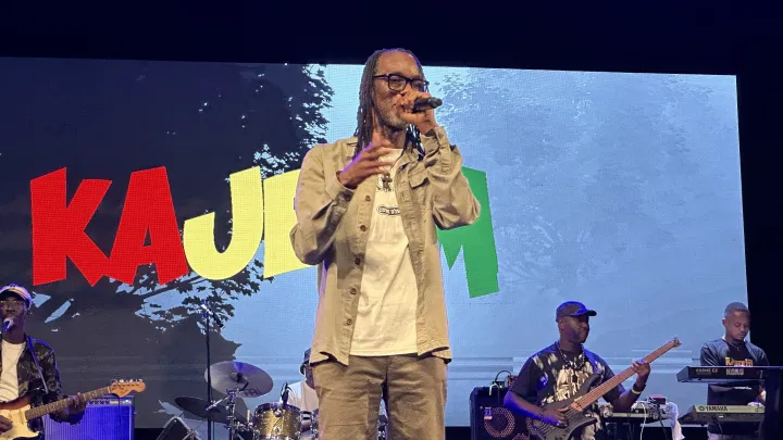 Image de Musique/Radio. Le samedi 12 octobre 2024, la salle Lougah François du Palais de la Culture d’Abidjan a vibré au rythme des sons reggae de Kajeem. L’artiste, emblématique figure du reggae ivoirien, a offert une performance riche en émotions, marquée par la tristesse suite à la disparition soudaine de son ami et collègue, Général Dimitri, qui devait partager la scène avec lui ce soir-là. Ce concert a été un hommage, un message d’éveil de conscience, et une démonstration de la résilience d’un artiste face à l’adversité. Retour sur une soirée qui restera gravée dans les mémoires. Le coup de tonnerre : un concert sous le signe du deuil et de l'hommage Ce samedi soir, le public abidjanais s'était rassemblé au Palais de la Culture pour célébrer la musique reggae et retrouver Kajeem, artiste reconnu pour sa capacité à marier des textes engagés avec des sonorités entraînantes. Mais dès l’ouverture du concert, l'ambiance a pris une tournure particulière. Kajeem, visiblement ému, a pris la parole pour annoncer une nouvelle qui a fait l'effet d'un coup de tonnerre. Général Dimitri, son ami et l’un des artistes invités à partager la scène avec lui ce soir-là, venait de décéder. « J’ai appris le décès de mon ami. Il devait même prester avec moi ce soir. Ce genre de nouvelle est vraiment difficile, surtout pour les personnes émotives comme moi », a confié Kajeem, sa voix marquée par l’émotion, avant de retenir ses larmes devant un public silencieux, profondément touché par cette annonce. « Mais nous allons faire ce concert pour lui rendre hommage », a-t-il ajouté, déterminé à transformer ce moment de tristesse en un hommage vibrant à son collègue disparu. Les spectateurs, émus par ces paroles, ont réagi par de chaleureux applaudissements, en signe de soutien et de réconfort. Cet instant a marqué le début d'une soirée où la musique est devenue un moyen de résilience, une façon de célébrer la vie malgré la douleur de la perte. Après ce moment de recueillement et de mélancolie, Kajeem a su trouver l'énergie nécessaire pour offrir à son public une prestation mémorable. Fidèle à son style, il a plongé les spectateurs dans un véritable voyage à travers ses titres emblématiques, alliant messages engagés et mélodies envoûtantes. Parmi les moments forts du concert, l'interprétation de la chanson « Le pays des merveilles », réalisée en duo avec Joëlle Bonee, a particulièrement marqué les esprits. Joëlle Bonee, bien connue dans le monde de la musique World en Côte d’Ivoire, a apporté sa voix puissante et son énergie communicative à ce titre emblématique de Kajeem. Leur duo a fait résonner dans la salle un message d’éveil de conscience et d'espoir, un appel à la réflexion sur les réalités sociales et politiques du pays, porté par des harmonies puissantes et une émotion palpable. La complicité entre les deux artistes, visible à chaque note, a su toucher le public et l'emmener dans ce qu'on pourrait appeler un « pays des merveilles », un espace où la musique devient un vecteur de réflexion et de prise de conscience. Le reggae, ce genre musical qui porte en lui un message de lutte, de liberté et de justice, a été le fil conducteur de cette soirée. Kajeem, à travers ses paroles et sa voix, a su rappeler à son public que la musique n’est pas seulement une source de divertissement, mais aussi un outil de changement social et de mobilisation. Ses chansons, pleines de poésie et de vérité, ont été un moyen de redonner de l'espoir, même dans un moment aussi sombre que celui de la disparition d’un être cher. Une « good vibe » qui rassemble et transcende les émotions Après l’émotion suscitée par l’annonce du décès de Général Dimitri, Kajeem a su ramener le sourire sur les visages de ses fans. En enchaînant des titres chantés en vernaculaire, il a réussi à embarquer son public dans une atmosphère de « good vibe », propre aux soirées reggae, où la musique devient un espace de partage et de communion. La salle Lougah François s'est alors transformée en un lieu de célébration, où les spectateurs ont dansé, chanté, et vécu un moment de joie collective. Ces chansons, inspirées des traditions locales et interprétées dans les langues vernaculaires, ont résonné avec une intensité particulière. Elles ont évoqué des souvenirs, des histoires, et ont permis au public de se reconnecter avec ses racines. C’était un moment de communion où la musique, dans toute sa simplicité et son authenticité, a rapproché les gens, leur permettant d'oublier, ne serait-ce que pour quelques heures, les difficultés de la vie quotidienne. Parmi les titres interprétés, certains ont particulièrement retenu l’attention, notamment ceux évoquant des scènes de vie typiques de l’Afrique, comme les animations claires de lune, moments de partage au sein des communautés. Kajeem a su recréer cette atmosphère chaleureuse, plongeant les spectateurs dans une sorte de nostalgie heureuse, qui a suscité à la fois des rires et des larmes. Cette « good vibe », caractéristique des concerts de Kajeem, a permis de transformer cette soirée en un événement unique, où chaque spectateur a pu se sentir partie intégrante d'une communauté unie par la musique. Le concert de Kajeem n'a pas seulement été une performance artistique : il a également été un hommage à l’amitié et à la résilience. En dépit de la tristesse causée par la disparition de son ami, Kajeem a trouvé la force de monter sur scène et de partager sa musique avec son public. Ce geste de bravoure a été salué par tous ceux présents, qui ont vu en lui un exemple de force et de détermination. En rendant hommage à Général Dimitri par sa musique, Kajeem a montré que l'art peut être une source de réconfort et un moyen de surmonter la douleur. Le reggae, avec ses rythmes envoûtants et ses paroles engagées, a servi de support à cet hommage. À travers chaque chanson, Kajeem a rappelé l’importance de la solidarité et de l’amour, des valeurs essentielles dans un monde souvent marqué par les divisions et les conflits. Le public, sensible à ce message, a répondu par des acclamations, des chants et des danses, faisant de ce concert un véritable moment de célébration de la vie. « Nous sommes ici ce soir pour célébrer la musique, célébrer l’amitié, et surtout, célébrer la vie, malgré les épreuves », a déclaré Kajeem en s’adressant à la foule. Ses paroles ont trouvé un écho particulier auprès des spectateurs, qui ont senti l’honnêteté et la sincérité de l’artiste dans chaque note, chaque mot. C’est cette authenticité, cette capacité à toucher le cœur des gens, qui a fait de cette soirée un moment inoubliable. La magie du reggae : un instrument de changement et d'unité Le reggae, genre musical né en Jamaïque et adopté à travers le monde, est connu pour ses messages de paix, de justice et de liberté. Kajeem, en tant que porte-voix du reggae en Côte d’Ivoire, a su utiliser cette musique pour transmettre des messages de sensibilisation et d’unité. Lors de ce concert, il a rappelé au public l’importance de rester unis face aux défis, de continuer à croire en un avenir meilleur, et de ne jamais perdre espoir. En interprétant des titres comme « Le pays des merveilles », Kajeem a invité les spectateurs à imaginer un monde meilleur, un monde où la paix et la justice prévalent. Son duo avec Joëlle Bonee a été l’un des moments les plus émouvants de la soirée, une véritable ode à la beauté de l’Afrique et à la force de ses peuples. Leur performance, empreinte de poésie et de passion, a montré que la musique est un moyen puissant de résister à l'adversité et de construire un avenir plus juste. Au-delà de l’hommage à son ami disparu, Kajeem a voulu faire de ce concert une véritable célébration de l’Afrique, de sa diversité culturelle, et de sa richesse humaine. Pour lui, la musique est un instrument de changement, un moyen de sensibiliser les consciences et de rassembler les peuples. Cette vision de la musique comme vecteur de transformation sociale a été au cœur de son concert, et a touché le public, qui a répondu avec enthousiasme et émotion. L’un des éléments clés qui a fait la réussite de cette soirée a été l’implication du public. Dès les premiers accords de musique, les spectateurs ont été embarqués dans un voyage où rires, larmes et réflexions se sont entremêlés. Les applaudissements nourris, les chants repris en chœur, et les danses improvisées ont montré à quel point le public était en phase avec l’artiste et les messages qu’il voulait transmettre. La présence de spectateurs de tous âges et de toutes origines a également contribué à créer une ambiance particulière. Des jeunes venus découvrir le reggae aux plus anciens, nostalgiques des premières heures de ce genre musical, chacun a trouvé dans ce concert une raison de se réjouir. La diversité du public a reflété celle des messages portés par Kajeem, et a montré que la musique, lorsqu’elle est sincère et authentique, peut rassembler au-delà des différences. « Ce concert a été bien plus qu’un simple spectacle, c’était un moment de partage, d’émotions et d’humanité », a confié un spectateur à l’issue de la soirée. Pour beaucoup, ce concert restera gravé dans les mémoires comme un moment où la musique a permis de transcender la tristesse et de retrouver, le temps d’une soirée, la force de sourire et de croire en un avenir meilleur. Alors que la soirée de Kajeem au Palais de la Culture d’Abidjan s'est terminée sous les applaudissements et les acclamations, une question demeure : dans un monde souvent marqué par l'adversité et la douleur, la musique peut-elle être un véritable vecteur d'espoir et de changement ? Peut-elle, à elle seule, créer les conditions nécessaires à l'unité et à la résilience des peuples ?