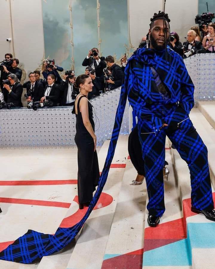 Image de Célébrités. Le talentueux artiste chanteur Nigérian, Burna Boy, a eu l'honneur comme certains de ses compatriotes tels que Tems et Skepta, à être invité au prestigieux gala Met qui s'est tenu ce lundi 1er mai à New York. Il faut dire que le thème de ce gala était Karl Lagerfeld en hommage au célèbre homme de la mode décédé en 2019. Pour dire vrai, ce qui a attiré l'attention des uns et des autres chez Burna Boy c'est plutôt la tenue avec une traîne qu'à arborer la méga star africaine. Je vous laisse découvrir sa tenue et ne manquez pas de me laisser vos impressions.