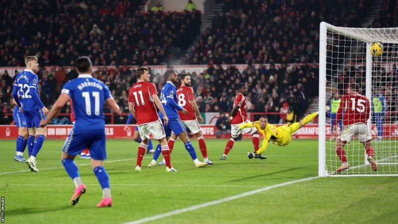 Image de Football. La victoire éclatante de l'Everton, dirigée par la grève clinique de Dwight McNeil, a non seulement donné une bouffée d'air frais à l'équipe mais a également marqué un tournant significatif dans leur parcours en Premier League. Dans un affrontement tendu contre Nottingham Forest, McNeil a inscrit son premier but de la saison avec une demi-volée nette au poteau arrière du City Ground. Cette victoire, associée à la défaite de Burnley 5-0 contre Sheffield United, a propulsé l'Everton de la dernière place à la 18e place du classement, illustrant la rapidité avec laquelle le paysage de la Premier League peut changer. Sean Dyche, le manager d'Everton, a souligné l'importance de cette victoire et a noté les progrès réalisés par son équipe après avoir été confrontée à une situation difficile en début de saison. "C'est un pas dans la bonne direction, mais il y a encore beaucoup à faire", a déclaré Dyche dans une interview à BBC Match of the Day. "Nous avons une saison solide malgré les dernières semaines difficiles. Nous avons atteint 14 points relativement tôt, et 17 auraient été un rendement assez sain. Bien sûr, cela a changé avec la déduction de points, mais la mentalité et les niveaux de performance sont corrects. Nous semblons être une équipe améliorée." La performance tenace d'Everton contre Forest a également mis en lumière le défi auquel est confronté l'entraîneur de Forest, Steve Cooper, après des défaites consécutives à domicile. Cooper, applaudissant généreusement par les supporters de Forest avant le coup d'envoi, se retrouve maintenant sous pression pour remonter le moral de son équipe et inverser leur série de résultats négatifs. Le match lui-même était plein de rebondissements, avec le gardien d'Everton, Jordan Pickford, réalisant des arrêts cruciaux pour préserver la victoire. La marge aurait pu être plus grande pour Everton, mais des opportunités manquées et des sauvetages de dernière minute de la part de Forest ont maintenu le suspense jusqu'au coup de sifflet final. La déduction de 10 points infligée à Everton pour violation des règles financières a ajouté une couche de complexité à leur saison, mais la réaction de l'équipe sur le terrain suggère une unité renforcée et une détermination à surmonter l'adversité. Le choix de Dyche de faire confiance à des joueurs tels que Beto, en l'absence de Dominic Calvert-Lewin, a suscité des moments de tension, mais la frappe impressionnante de McNeil a finalement assuré la victoire. Du côté de Forest, la série de défaites consécutives à domicile soulève des questions sur la direction que prend l'équipe. La blessure de Taiwo Awoniyi, qui ne devrait pas revenir avant début 2024, ajoute également un défi supplémentaire à la capacité de l'équipe à marquer des buts. Alors que le football continue de nous réserver des surprises, ce match entre Everton et Forest a fourni un spectacle captivant. Les supporters ont exprimé leur joie après la victoire, tandis que les interrogations persistent sur la manière dont les deux équipes aborderont les prochaines étapes de la saison. Dans l'ensemble, cette victoire a-t-elle solidifié la position d'Everton pour surmonter la déduction de points et se maintenir en Premier League? Steve Cooper sera-t-il en mesure de remobiliser son équipe et de renverser leur récente série de défaites? Alors que la saison de Premier League se déroule, les réponses à ces questions continueront d'influencer le destin des équipes impliquées. Quelles sont vos réflexions sur ce match et ses implications à long terme pour Everton et Nottingham Forest?