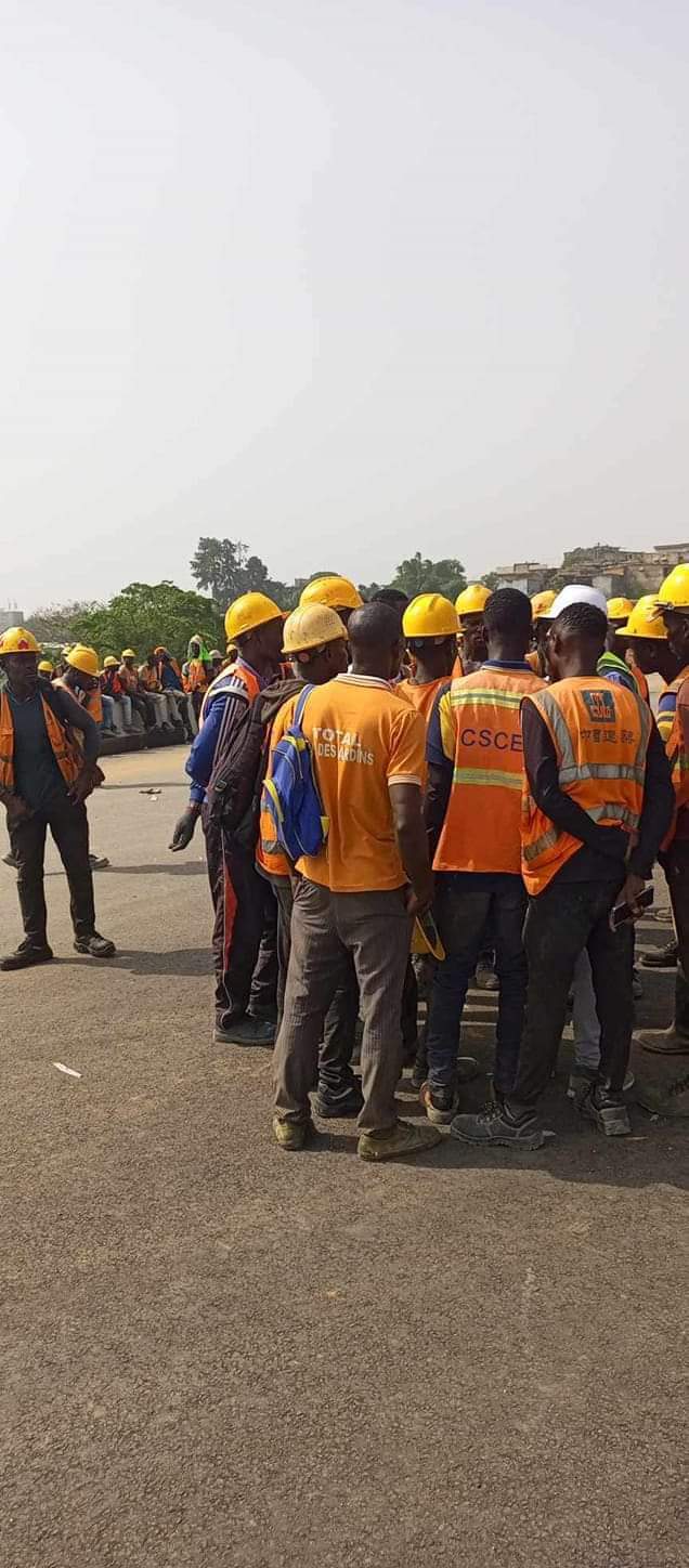 Image de Société. La crise qui secoue le chantier du 4ème pont d'Abidjan, reliant les communes de Yopougon et Plateau à travers Attéoubé et la lagune Ebrié, a atteint un point critique avec l'initiation d'une grève par les employés. Cette action découle de multiples revendications, principalement liées aux retards de paiement des salaires et à la quête de meilleures conditions de travail. L'impact de cette grève s'est fait ressentir de manière significative lors de la récente visite du Premier Ministre sur le chantier. Ce haut dignitaire, venu inspecter l'avancement des travaux et encourager l'équipe en charge du projet, s'est trouvé confronté à une atmosphère tendue et à des revendications exprimées bruyamment par les travailleurs en grève. Cette perturbation a incontestablement entaché la visite officielle et a souligné les problèmes préoccupants qui entravent l'avancement de ce projet majeur. La construction du 4ème pont d'Abidjan représente une entreprise colossale, non seulement en termes de logistique et d'ingénierie, mais aussi en importance stratégique pour la ville et le pays dans son ensemble. La liaison entre Yopougon et Plateau est cruciale pour améliorer la connectivité et réduire les embouteillages qui paralysent souvent la circulation dans cette métropole en pleine expansion. Cependant, ces ambitions louables sont désormais mises à mal par une série de problèmes persistants. Les ouvriers, se sentant lésés par des retards de paiement de leurs salaires, ont décidé de se mettre en grève pour attirer l'attention sur leurs conditions de travail précaires. Cette situation a également mis en lumière d'autres revendications telles que des heures supplémentaires non rémunérées, des questions de sécurité sur le chantier et un manque de mesures adéquates pour assurer le bien-être des travailleurs. La grève sur le chantier a des répercussions bien au-delà de la simple demande de paiement des salaires en retard. Elle soulève des questions plus larges concernant les normes de travail, les droits des employés et la gestion globale du projet. En perturbant la visite du Premier Ministre, cet incident a mis en évidence les tensions existantes et a posé un défi majeur aux autorités pour trouver une solution rapide et efficace. La réconciliation entre les parties prenantes est cruciale pour remettre le projet sur les rails. Il est impératif que les responsables gouvernementaux, les représentants syndicaux et les gestionnaires du chantier s'assoient autour de la table pour négocier des solutions concrètes. La résolution de ces problèmes requiert une approche équilibrée, prenant en compte à la fois les préoccupations légitimes des travailleurs et la nécessité de maintenir l'avancée des travaux pour le bien-être de la ville et de ses habitants. En parallèle, une réflexion plus approfondie sur les processus de paiement des salaires, les conditions de travail et la communication entre les parties impliquées dans ce projet de grande envergure est nécessaire. Il est crucial d'établir des mécanismes transparents et efficaces pour éviter de futures interruptions et assurer la progression régulière de la construction. Le 4ème pont d'Abidjan demeure une priorité incontestable pour la ville et le pays. Sa finalisation représente un jalon important pour l'infrastructure et le développement économique. Cependant, cette crise actuelle doit servir de catalyseur pour des changements significatifs et durables afin d'assurer le respect des droits des travailleurs, la bonne gestion du chantier et la réalisation réussie de ce projet crucial pour la Côte d'Ivoire.