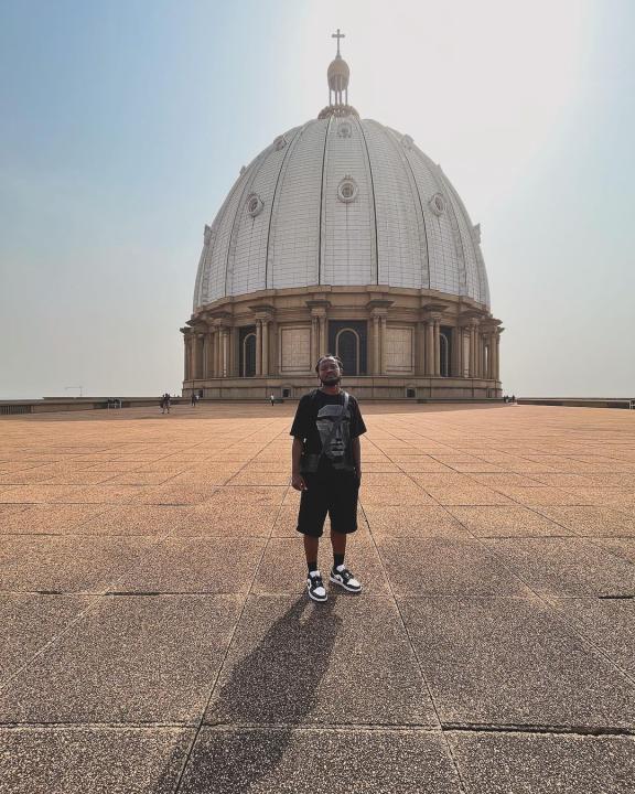 Image de Musique/Radio. Ange Freddy, l'humoriste, comédien, vidéaste et photographe ivoirien bien connu, a récemment dévoilé une nouvelle publication captivante. En préparation de la TotalEnergies CAF Coupe d'Afrique des Nations Côte d'Ivoire 2023, Ange Freddy s'est associé au sponsor officiel TotalEnergies CI pour présenter une expérience unique : la visite de la plus grande basilique du monde, la basilique Notre Dame de la Paix, située à Yamoussoukro, en Côte d'Ivoire. La basilique Notre Dame de la Paix, souvent comparée à la Basilique Saint-Pierre de Rome en termes de taille, est un chef-d'œuvre architectural situé au cœur de Yamoussoukro. Ange Freddy ne se contente pas de dévoiler les aspects impressionnants de l'édifice, mais il le fait avec sa touche distinctive d'humour qui rend la visite mémorable et divertissante. La publication, en collaboration avec TotalEnergies CI, revêt également une dimension particulière en lien avec la prochaine Coupe d'Afrique des Nations. Elle souligne la richesse culturelle de la Côte d'Ivoire tout en célébrant l'événement sportif à venir. Cette collaboration entre l'artiste polyvalent et le sponsor officiel offre une occasion unique de fusionner le divertissement, la culture et le sport.