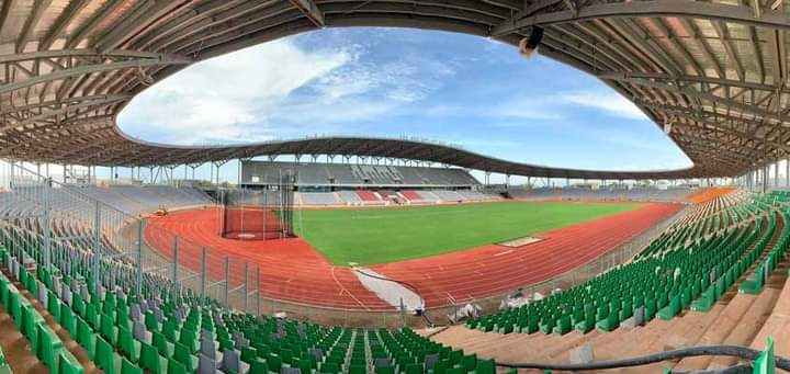 Image de Football. La Coupe d'Afrique des Nations (CAN) 2023, organisée en Côte d'Ivoire, représente un événement majeur dans le monde du football africain. Ce tournoi, rassemblant 24 équipes qualifiées, se déroule dans six stades stratégiquement répartis à travers le pays. Ces stades, chacun avec ses caractéristiques uniques et son histoire, sont le théâtre de confrontations spectaculaires, reflétant non seulement la passion du football mais aussi le développement infrastructurel en Côte d'Ivoire. Stade Alassane Ouattara Le stade Alassane Ouattara, également connu sous le nom de stade olympique d’Ebimpé, se distingue comme la pièce maîtresse de ce tournoi. Situé dans le village d’Ebimpé, au nord d'Abidjan, ce stade polyvalent symbolise la modernité et l'ambition sportive de la Côte d’Ivoire. Avec une capacité d'accueil de 60 000 places, il est non seulement le plus grand du pays mais aussi un des plus impressionnants du continent africain. L'inauguration du stade en octobre 2020 a marqué une étape importante dans la préparation de la CAN 2023. Conçu pour accueillir diverses disciplines sportives, il représente un investissement significatif dans les infrastructures sportives ivoiriennes et africaines. Lors de la CAN 2023, le stade Alassane Ouattara a accueilli le match d'ouverture ainsi que la finale, des moments clés qui ont captivé l'attention de millions de fans de football à travers le monde. Stade de Bouaké Le stade de Bouaké, rebaptisé stade de la Paix, est le deuxième plus grand stade de Côte d'Ivoire. Avec une histoire remontant à la CAN 1984, ce stade a subi d'importantes rénovations pour accueillir efficacement les matchs de la CAN 2023. Sa capacité a été augmentée à 40 000 places, offrant ainsi un cadre plus grand et plus moderne pour les compétitions. La rénovation du stade de Bouaké illustre la volonté du pays de revitaliser ses infrastructures sportives historiques. Ces améliorations incluent une pelouse de dernière génération, des installations médicales, des vestiaires modernes, et une salle de presse. Ces mises à niveau ont non seulement amélioré l'expérience pour les joueurs et les équipes, mais ont également augmenté le confort pour les spectateurs. Stade de Yamoussoukro ou Stade Charles Konan Banny Le stade de Yamoussoukro, également connu sous le nom de stade Charles Konan Banny, est un hommage à l'ancien Premier ministre de Côte d'Ivoire. Avec une capacité de 20 000 places, ce stade représente une partie importante de l'effort du pays pour étendre ses infrastructures sportives au-delà d'Abidjan. La construction du stade de Yamoussoukro, lancée en 2018 et achevée en 2021, démontre l'engagement de la Côte d'Ivoire à développer des installations sportives dans d'autres régions, favorisant ainsi une plus grande inclusion et participation au sport à travers le pays. Ce stade, situé dans la capitale politique, joue un rôle crucial dans la décentralisation des activités sportives, offrant une nouvelle destination pour les événements sportifs majeurs en Côte d'Ivoire. Stade Amadou Gon Coulibaly de Korhogo Le stade Amadou Gon Coulibaly, situé à Korhogo, dans le nord de la Côte d'Ivoire, est un autre exemple de l'expansion des infrastructures sportives du pays. Nommé en l'honneur de l'ancien Premier ministre, ce stade, avec une capacité de 20 000 places, a été construit spécifiquement pour la CAN 2023. Sa construction, qui a débuté en 2018 et s'est achevée en 2023, symbolise l'effort national pour amener des installations sportives de haute qualité dans toutes les régions du pays. Le stade Amadou Gon Coulibaly a non seulement servi pour les matchs du Groupe E de la CAN 2023 mais représente également un héritage durable pour la communauté de Korhogo, favorisant le développement du football et d'autres sports dans la région. Stade de San-Pedro Le stade de San-Pedro, nommé en l'honneur de la légende du football ivoirien Laurent Pokou, est situé dans la ville portuaire de San-Pedro. Avec une capacité de 20 000 places, ce stade est un des trois nouvellement construits pour la CAN 2023. Sa construction reflète la diversification géographique des infrastructures sportives en Côte d'Ivoire. En situant un stade moderne dans la région sud-ouest du pays, le gouvernement ivoirien montre son engagement à rendre le sport plus accessible à toutes les régions. Le stade de San-Pedro sert non seulement de lieu pour les matchs internationaux mais aussi comme un centre pour le développement du sport local. En somme, les stades de la CAN Côte d’Ivoire 2023 ne sont pas de simples lieux de compétition; ils symbolisent le progrès, l'unité et la passion pour le sport. Ils incarnent l’esprit du football africain et le désir de la Côte d’Ivoire de jouer un rôle central sur la scène sportive internationale. Alors que la Côte d'Ivoire continue de s'épanouir grâce à ces infrastructures, une question demeure : Comment ces stades et les événements qu'ils accueillent peuvent-ils continuer à influencer positivement le développement social et économique du pays dans les années à venir ?