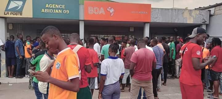 Image de Football. La poste d'Adjamé 220 est bien plus qu'un simple lieu de service postal dans la vie quotidienne des habitants d'Abidjan, Côte d'Ivoire. C'est un point névralgique où la passion pour le football et le soutien inébranlable envers l'équipe nationale, les Éléphants, se manifeste de manière frappante. L'effervescence qui règne à cet endroit est indéniablement liée à l'enthousiasme des supporters qui se pressent pour s'offrir des tickets en vue du prochain match tant attendu. Les rues animées d'Adjamé servent de toile de fond à cette scène dynamique, où les supporters se rassemblent avec l'espoir palpable de voir leurs héros nationaux fouler le terrain. L'atmosphère est électrique, chargée d'une énergie positive qui unit les individus autour d'une cause commune : le soutien fervent à l'équipe de football nationale. Les discussions enflammées sur les performances passées et les pronostics pour le prochain match résonnent dans l'air, créant un sentiment d'unité parmi les supporters. À l'intérieur de la poste d'Adjamé 220, les guichets habituellement dédiés aux services postaux se transforment en points de vente improvisés pour les billets du match des Éléphants. Les employés de la poste, habitués à traiter des colis et des lettres, se retrouvent désormais à jouer un rôle crucial dans la distribution des billets et à gérer l'afflux constant de supporters passionnés. La transition temporaire de cet espace postal en un centre de distribution de billets de football souligne l'importance culturelle du sport dans la vie quotidienne des habitants. Les supporters, vêtus des couleurs vives de l'équipe nationale, forment une file d'attente qui s'étend bien au-delà de l'entrée de la poste. Le brouhaha joyeux des discussions et des chants de soutien crée une ambiance festive, transformant temporairement la poste en un lieu de célébration collective. Les enfants, les jeunes et les adultes partagent cet esprit communautaire, renforçant ainsi les liens sociaux au-delà des différences individuelles. Certains supporters arrivent munis de drapeaux, de tambours et d'autres accessoires festifs pour exprimer leur dévouement envers l'équipe nationale. Ces éléments visuels ajoutent une dimension artistique à l'événement, transformant la poste en une galerie temporaire où les symboles nationaux et les expressions créatives des supporters convergent pour célébrer l'identité collective. Les moments de tension surviennent lorsque la demande de billets dépasse l'offre disponible. Des discussions animées et des négociations passionnées éclatent entre les supporters déterminés à obtenir leur précieux sésame pour le match à venir. Certains font preuve de créativité pour persuader les autres de céder leur place dans la file d'attente, tandis que d'autres partagent des anecdotes mémorables liées à leur passion pour les Éléphants. Ces interactions ajoutent une dimension humaine à l'expérience, soulignant l'impact émotionnel profond que le football a sur la vie des supporters. Les réseaux sociaux amplifient encore l'excitation palpable à la poste d'Adjamé 220. Des photos et des vidéos des supporters attendant patiemment leurs billets inondent les plateformes en ligne, créant une véritable frénésie virale. Les hashtags liés au match deviennent des tendances locales, renforçant la connectivité numérique entre les supporters et étendant l'expérience au-delà des limites physiques de la poste. En conclusion, la poste d'Adjamé 220 se transforme en un théâtre vibrant où la passion pour le football et le soutien indéfectible envers l'équipe nationale des Éléphants transcendent les fonctions habituelles de cet espace. C'est un lieu où la communauté se rassemble, où les liens sociaux se renforcent et où l'excitation pour le prochain match crée une atmosphère unique et mémorable. Au-delà des transactions postales ordinaires, la poste d'Adjamé 220 devient un symbole vivant de la façon dont le sport peut fusionner avec la vie quotidienne pour créer des moments d'unité et de célébration.