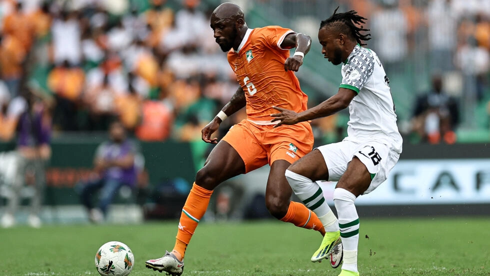 Image de Football. L'ascension fulgurante de Seko Fofana dans le football international et son impact sur la sélection ivoirienne soulèvent des questions fascinantes sur la dynamique des équipes nationales, le patriotisme dans le sport, et la gestion des carrières entre clubs et sélections nationales. L’histoire de Fofana avec la Côte d'Ivoire est un parfait exemple de ces enjeux. Le parcours de Fofana reflète la complexité de l'identité et de la nationalité dans le football moderne. Né en France et ayant joué pour les équipes de jeunes françaises, il fait le choix de représenter la Côte d'Ivoire, pays d'origine de ses parents, à l'âge adulte. Ce choix illustre la dualité des identités que beaucoup de joueurs doivent naviguer, une décision souvent chargée émotionnellement et influencée par des facteurs tant personnels que sportifs. La gestion de sa carrière entre son club et la sélection nationale met également en lumière les défis auxquels les joueurs africains sont souvent confrontés. Le refus de Fofana de participer à la CAN 2021 pour privilégier son club soulève des questions sur la pression exercée par les clubs européens sur leurs joueurs africains, et sur le conflit potentiel entre les ambitions en club et les responsabilités nationales. Ses performances impressionnantes avec la Côte d'Ivoire lors de la CAN 2024 témoignent de son immense talent. Sa capacité à dominer le milieu de terrain, à se projeter vers l'avant et à défendre avec acharnement, rappelle les grandes figures du football ivoirien comme Yaya Touré. Son style de jeu "box-to-box" est crucial pour l'équilibre et la dynamique de l'équipe, faisant de lui un élément central du système de jeu de Jean-Louis Gasset. Cependant, la réaction mitigée à sa performance contre le Nigeria souligne la pression immense et parfois les attentes irréalistes placées sur les épaules des joueurs vedettes. Cette situation est symptomatique d'une tendance plus large dans le sport de haut niveau, où les succès sont souvent glorifiés et les échecs sévèrement critiqués. La capacité de Fofana à gérer cette pression sera cruciale non seulement pour son développement personnel mais aussi pour l'avenir de la sélection ivoirienne. La présence de Fofana dans l'équipe ivoirienne a également un impact plus large sur la dynamique de l'équipe. Son retour et ses performances peuvent inspirer ses coéquipiers, élever le niveau de jeu de l'équipe, et apporter un sentiment d'unité et de fierté nationale. En outre, son histoire peut servir de modèle pour les jeunes joueurs ivoiriens et africains qui aspirent à réussir tant au niveau national qu'international. En définitive, le parcours de Seko Fofana avec la Côte d'Ivoire est révélateur de nombreux aspects du football moderne : la dualité de l'identité nationale, la gestion des carrières entre les clubs et les équipes nationales, la pression et les attentes placées sur les joueurs vedettes, et l'impact d'un joueur clé sur l'ensemble d'une équipe. Alors que la Côte d'Ivoire continue son parcours dans la CAN 2024, avec Fofana comme figure de proue, elle porte les espoirs et les attentes d'une nation. Dans ce contexte, une question ouverte demeure : comment les fédérations nationales et les clubs peuvent-ils mieux collaborer pour soutenir les carrières des joueurs tout en respectant leurs engagements nationaux et personnels ?