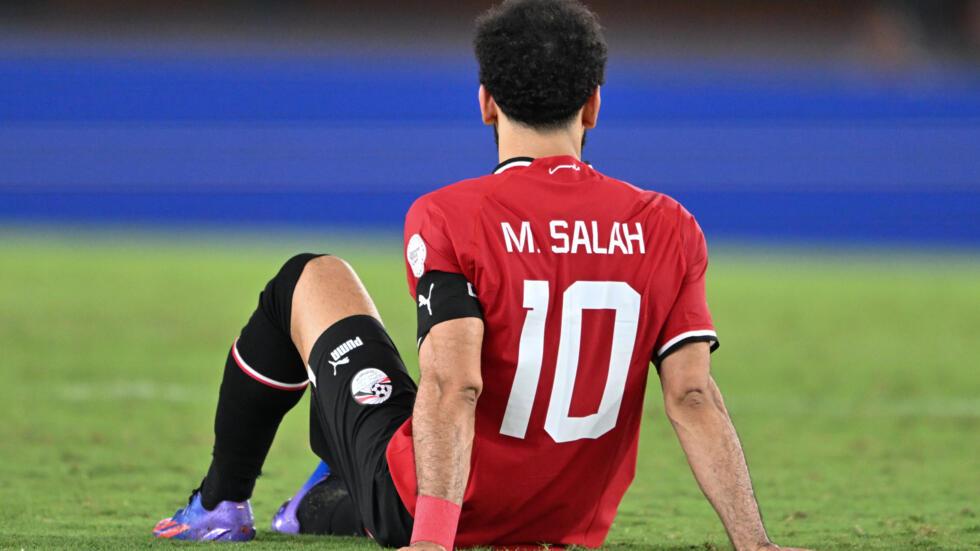 Image de Football. Mohamed Salah, l'attaquant de Liverpool, demeure confiant quant à sa capacité à conduire l'Égypte vers la victoire à la Coupe d'Afrique des Nations, affirmant que cela se produira "tôt ou tard". Malheureusement, une blessure aux ischio-jambiers survenue lors du match contre le Ghana le privera de participer aux deux prochains matchs de son équipe. Pour assurer leur qualification dans le groupe, les Pharaons doivent remporter leur dernier match contre le Cap-Vert. Malgré ses succès avec Liverpool, où il a remporté la Premier League et la Ligue des Champions, Salah n'a pas encore connu le triomphe au niveau national. Ses précédentes expériences en Coupe d'Afrique ont été marquées par des déceptions, avec des défaites contre le Sénégal en 2022 et le Cameroun en 2017. Salah a fait sa première apparition en équipe nationale en 2011, un an après la septième victoire record de l'Égypte en Coupe des Nations. Lors de ce match, son équipe a eu besoin de son penalty pour arracher un match nul contre le Mozambique. Même après sa sortie en raison d'une blessure, l'équipe a réussi à revenir deux fois contre le Ghana. La prochaine étape cruciale pour l'Égypte est le match contre le Cap-Vert, qui déterminera leur qualification pour les huitièmes de finale. Actuellement en tête du groupe B, le Cap-Vert présente un défi redoutable. Salah, bien que blessé, reste optimiste quant aux chances de son équipe. Il souligne l'importance de rester concentré et de faire preuve de détermination pour surmonter les obstacles. La blessure de Salah demeure une préoccupation, mais il met en avant l'importance du prochain match. Malgré les difficultés actuelles, il exprime sa confiance envers l'équipe, soulignant la qualité des joueurs et du coach. Il insiste sur le travail acharné comme clé du succès, affirmant que la qualification dépend simplement de la victoire dans un match, à partir duquel ils pourront construire leur parcours. Alors que l'Égypte aspire à se qualifier pour les huitièmes de finale, Salah souligne la positivité au sein de l'équipe. Il met en avant la grandeur de l'équipe et appelle à la persévérance et à la détermination pour surmonter les défis à venir. La route vers le triomphe peut être difficile, mais Salah croit en la possibilité de tout accomplir avec un travail acharné et une équipe solide. En conclusion, la détermination de Mohamed Salah à remporter la Coupe d'Afrique des Nations demeure inébranlable malgré les obstacles. Alors que l'Égypte se prépare pour des rencontres cruciales, la question qui persiste est la suivante : l'équipe parviendra-t-elle à surmonter les défis et à réaliser le rêve de Salah "tôt ou tard" ?